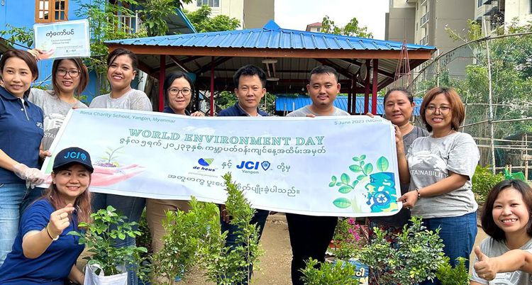 a group of people are holding a vinyl sheet in front of nurturing plants.